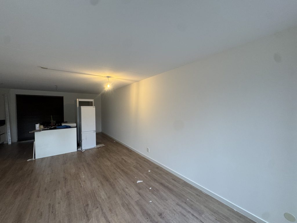 Lange woonkamer in een nieuwe woning met een strak gesausde witte wand en een open keuken